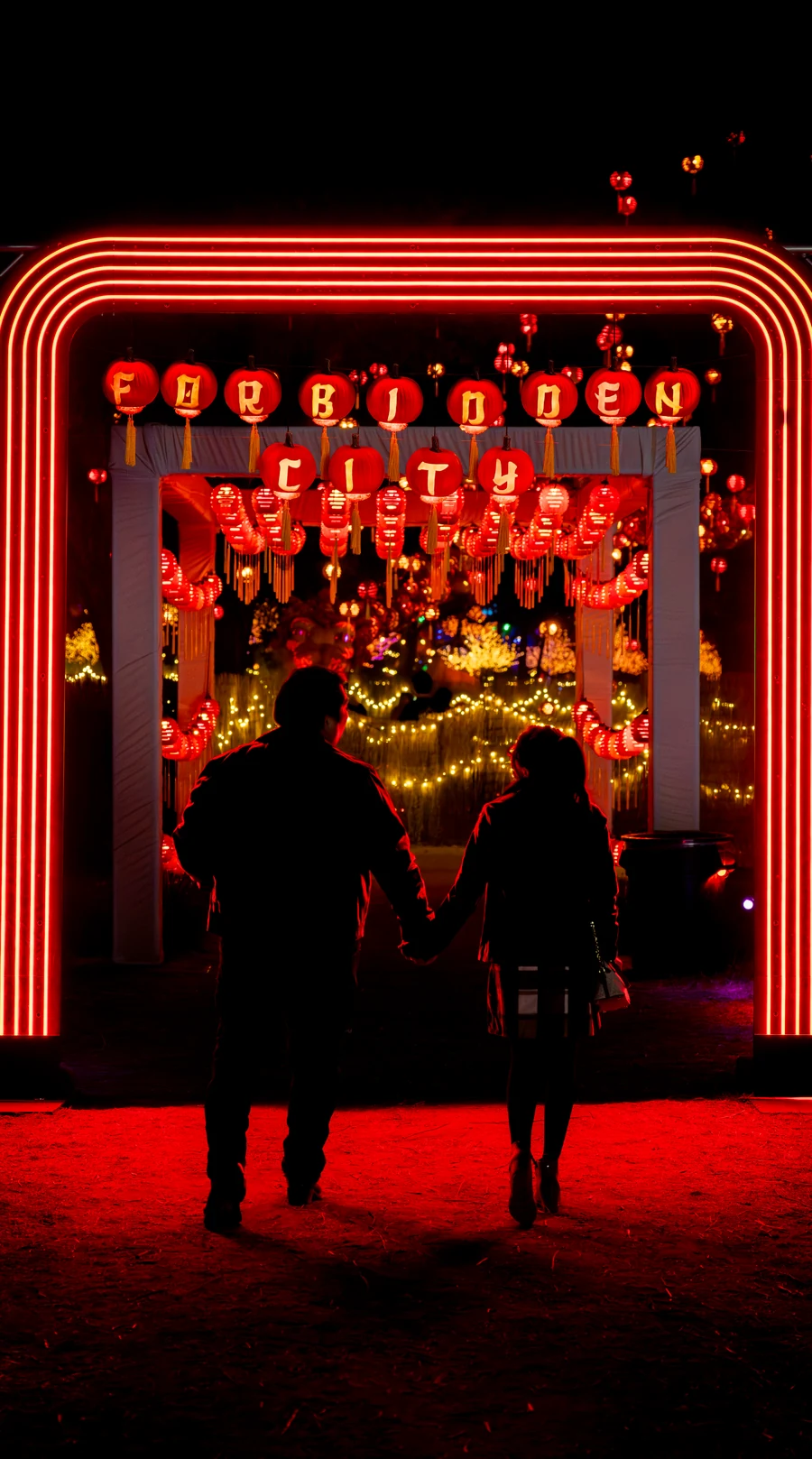 A couple holding hands beneath the glowing Forbidden City arch