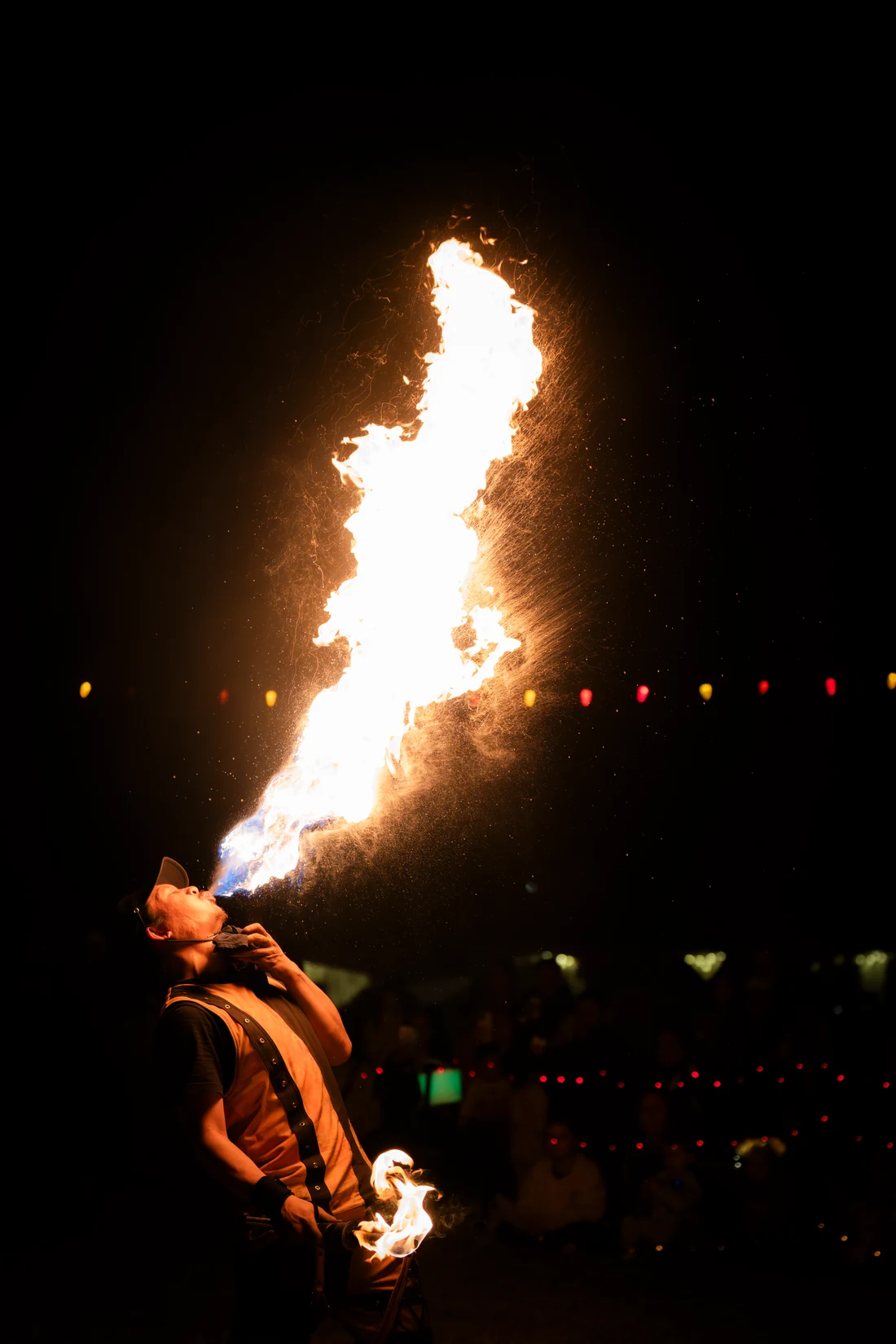 A fire performer breathing a tall column of flame above the crowd
