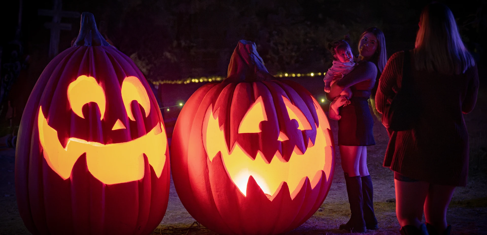 Two giant carved jack-o'-lanterns glowing beside guests on the trail